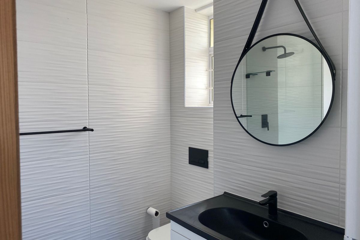 Modern bathroom featuring textured white wall tiles, a sleek black vanity basin with matching fixtures, and a wall-mounted toilet.