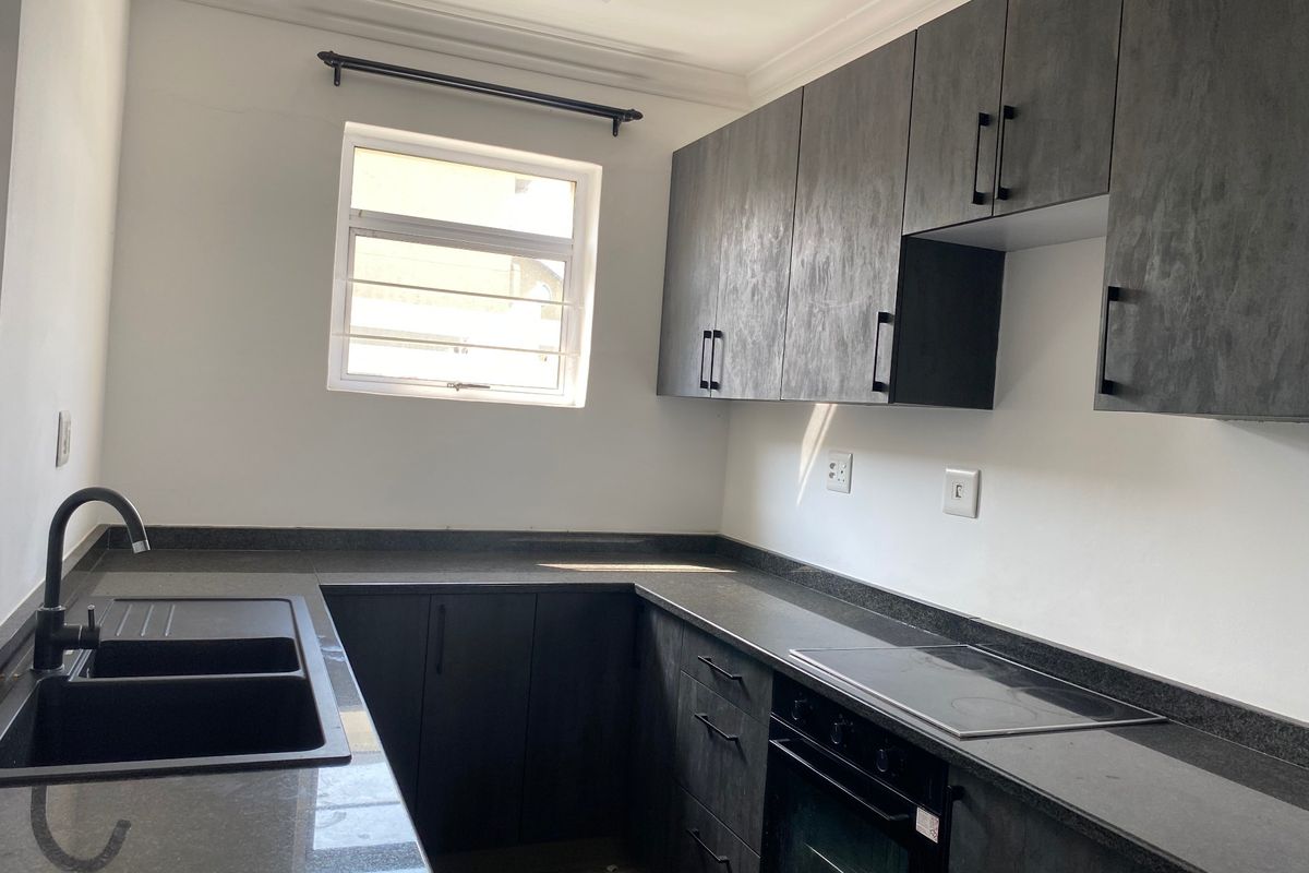Modern kitchen featuring dark cabinetry, stone countertops, integrated electric hob, built-in oven, and a double basin sink with a contemporary black mixer tap.