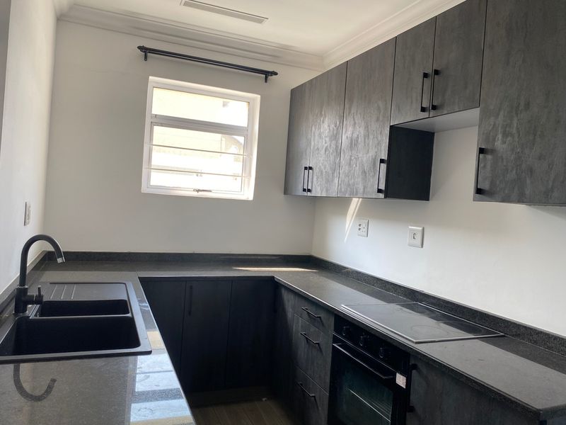 Modern kitchen featuring dark cabinetry, stone countertops, integrated electric hob, built-in oven, and a double basin sink with a contemporary black mixer tap.
