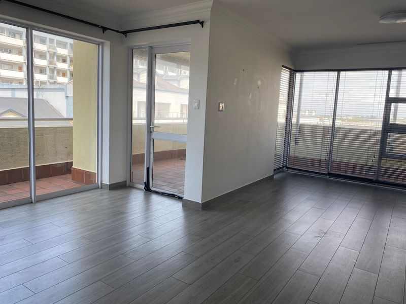 An empty, light-filled living area featuring modern laminate flooring, large sliding glass doors, and access to an outdoor balcony space.