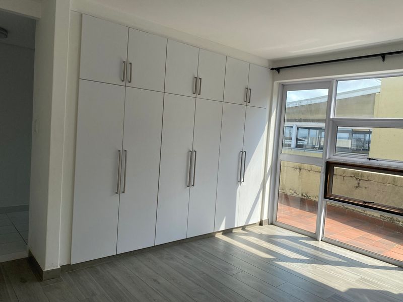 Bright bedroom featuring extensive floor-to-ceiling built-in cupboards, modern laminate flooring, and direct access to an outdoor balcony area.