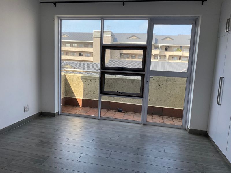 An empty bedroom featuring modern laminate flooring, built-in cupboards, and direct access to a private balcony with exterior views.