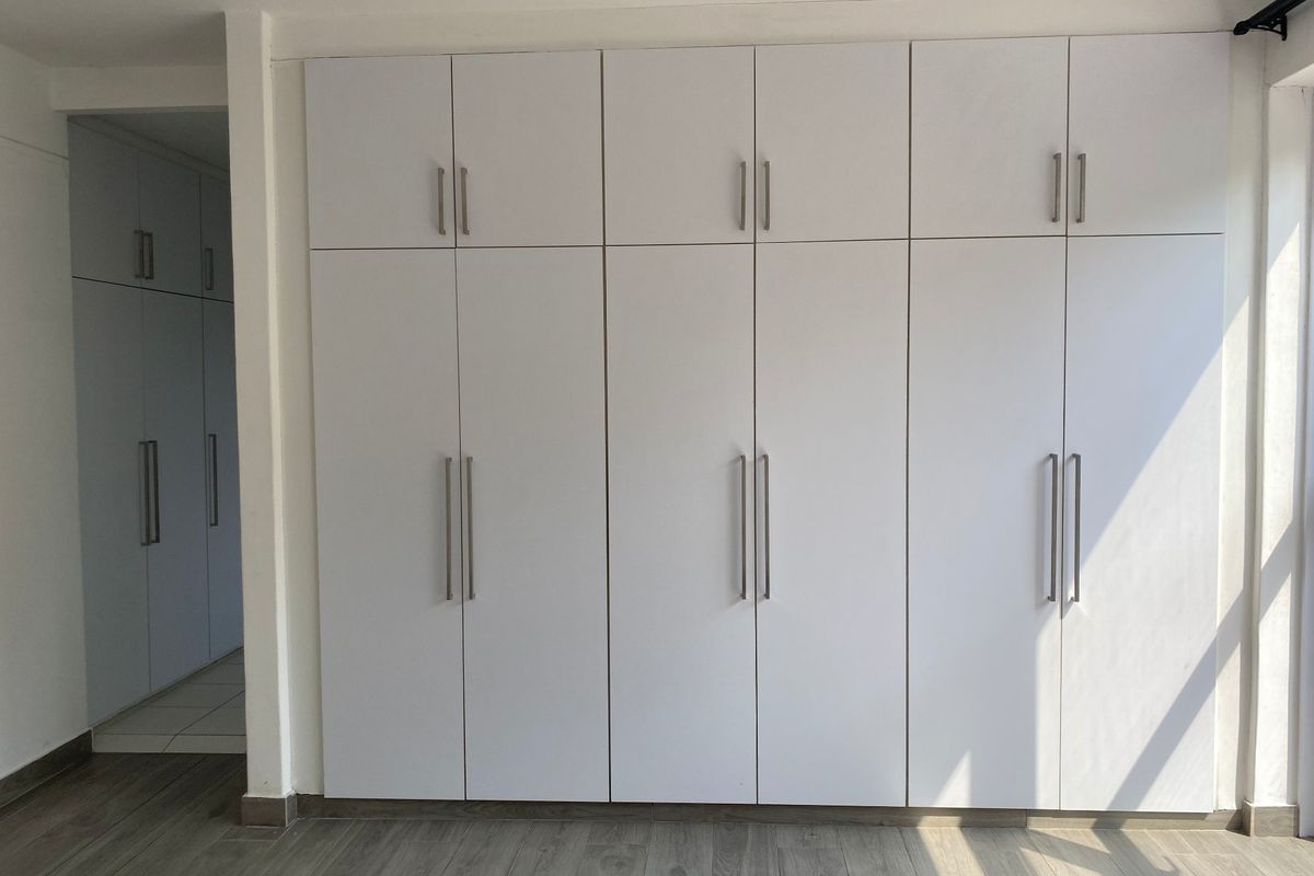 A bright bedroom featuring extensive floor-to-ceiling built-in cupboards with modern handles and durable laminate flooring.