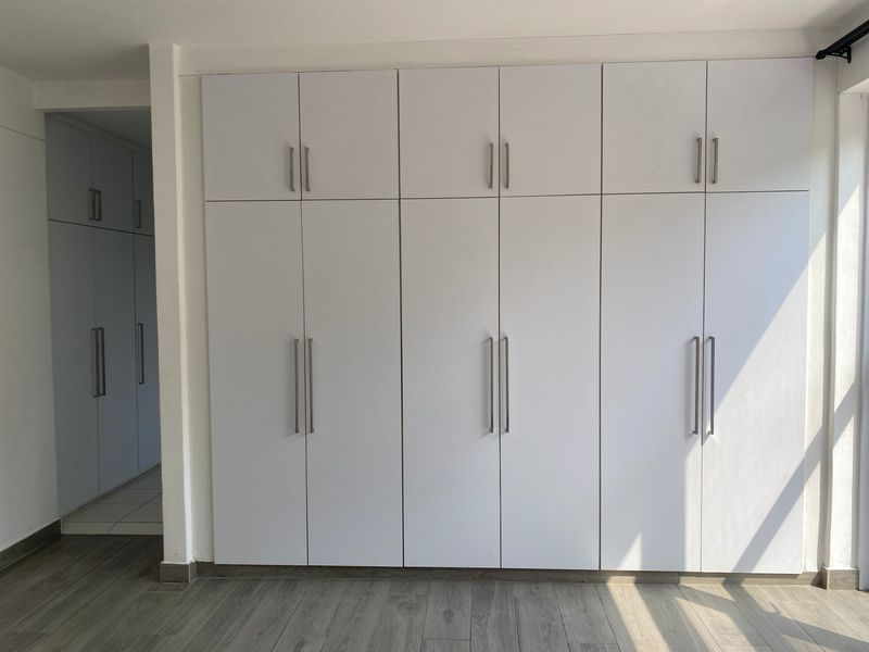 A bright bedroom featuring extensive floor-to-ceiling built-in cupboards with modern handles and durable laminate flooring.