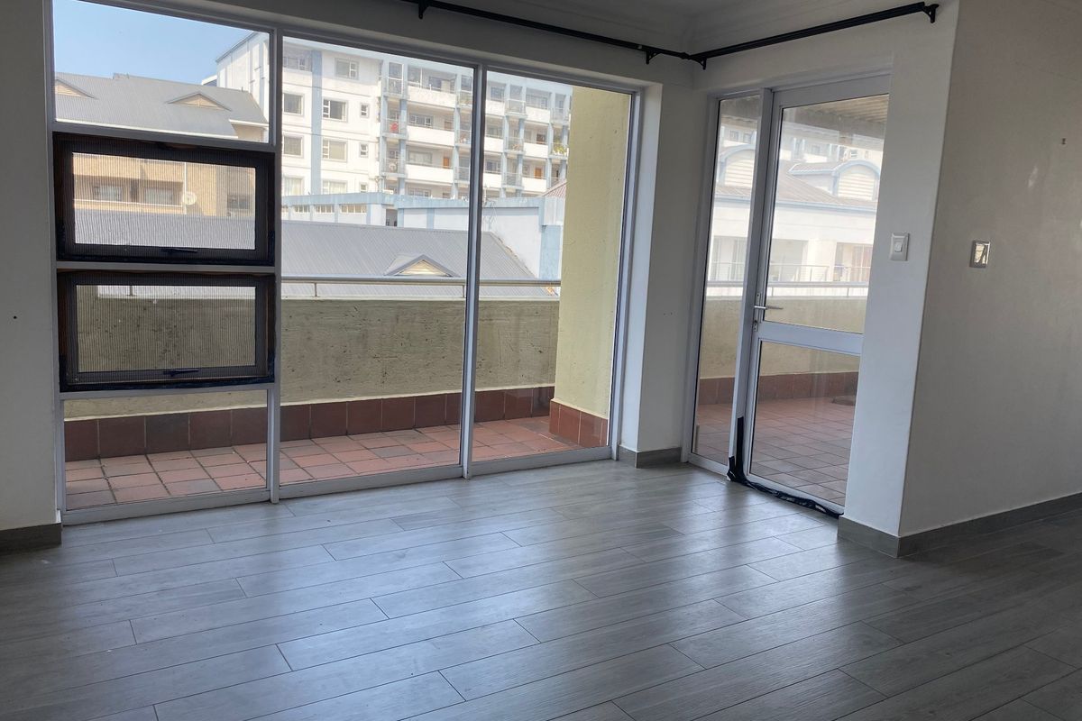 Bright and spacious living area featuring modern laminate flooring and large sliding glass doors providing direct access to an outdoor balcony.