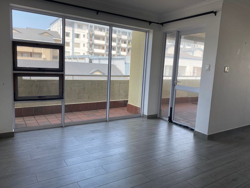 Bright and spacious living area featuring modern laminate flooring and large sliding glass doors providing direct access to an outdoor balcony.