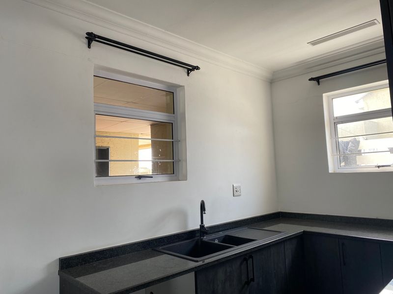 A clean, modern kitchen featuring dark cabinetry, granite countertops, a double sink with a black mixer tap, and security bars on the windows.