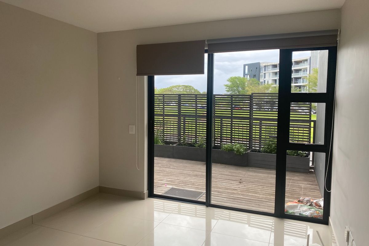 An empty living area featuring large sliding glass doors that open onto a private wooden deck with a privacy screen.