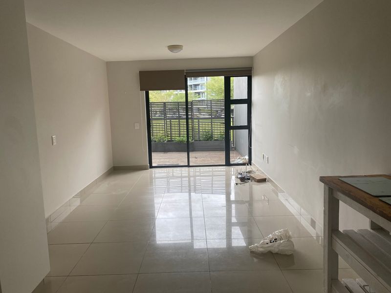 An empty, open-plan living area featuring neutral tiled flooring and a large sliding glass door providing access to an outdoor patio space.