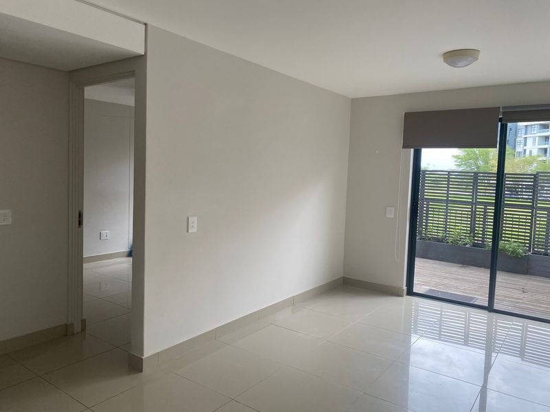 A bright, empty living area featuring neutral tiled flooring, clean walls, and a sliding glass door providing access to an outdoor patio space.