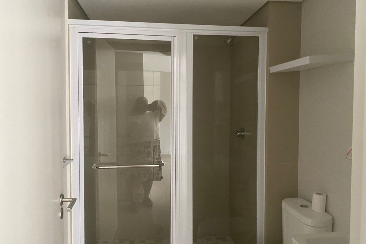 A clean, modern bathroom featuring a glass-enclosed shower, a standard toilet, and a wall-mounted shelf, presenting a functional and well-maintained space.