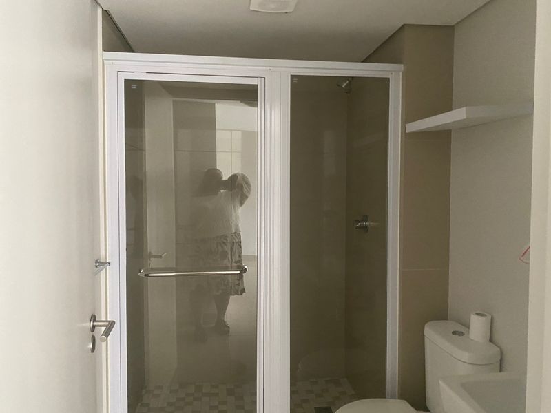 A clean, modern bathroom featuring a glass-enclosed shower, a standard toilet, and a wall-mounted shelf, presenting a functional and well-maintained space.
