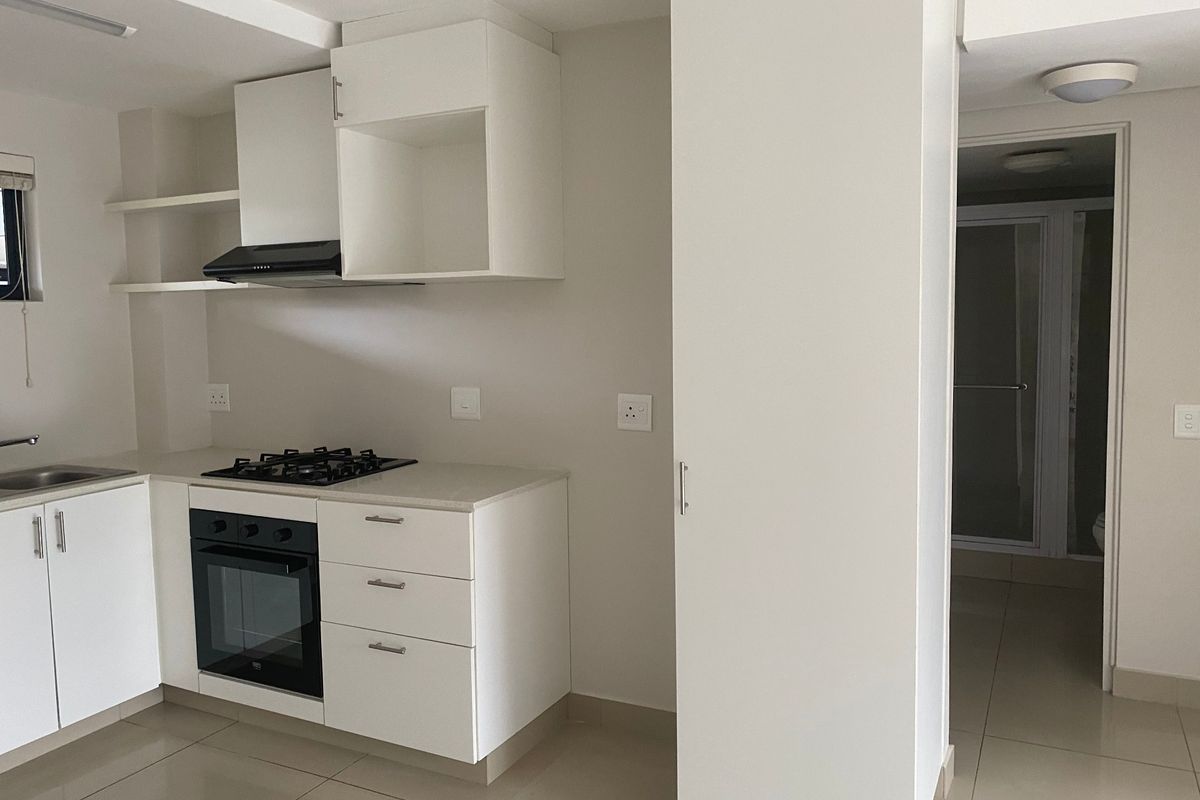 A clean, modern kitchen featuring white cabinetry, stone countertops, a gas hob, and an integrated oven, with tiled flooring throughout.