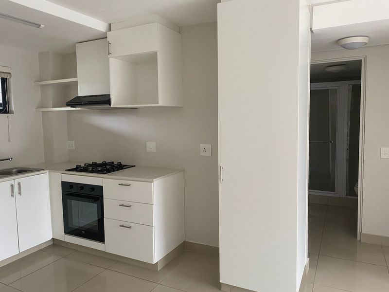 A clean, modern kitchen featuring white cabinetry, stone countertops, a gas hob, and an integrated oven, with tiled flooring throughout.