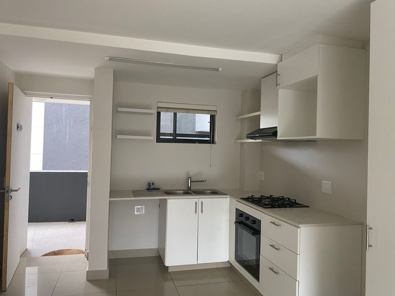 A clean, modern kitchen featuring white cabinetry, stone countertops, a gas hob, built-in oven, and extractor fan, with direct access to an outdoor balcony.
