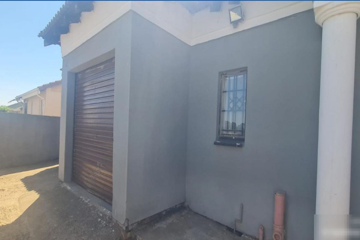 Rear exterior view of the property featuring a roller shutter garage door, security window bars, and external wall lighting.