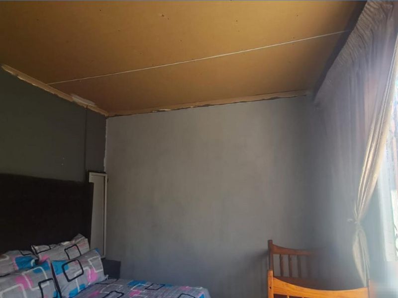 A bedroom featuring a window with a security gate and basic ceiling paneling, requiring cosmetic updates to improve the overall finish.