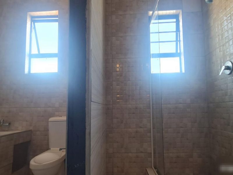 A tiled bathroom featuring a shower enclosure, built-in vanity, and toilet, with natural light provided by two casement windows.