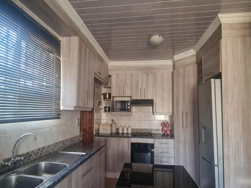 A functional kitchen featuring wood-look cabinetry, granite-style countertops, a double sink, and integrated appliances including an oven, hob, and extractor fan.