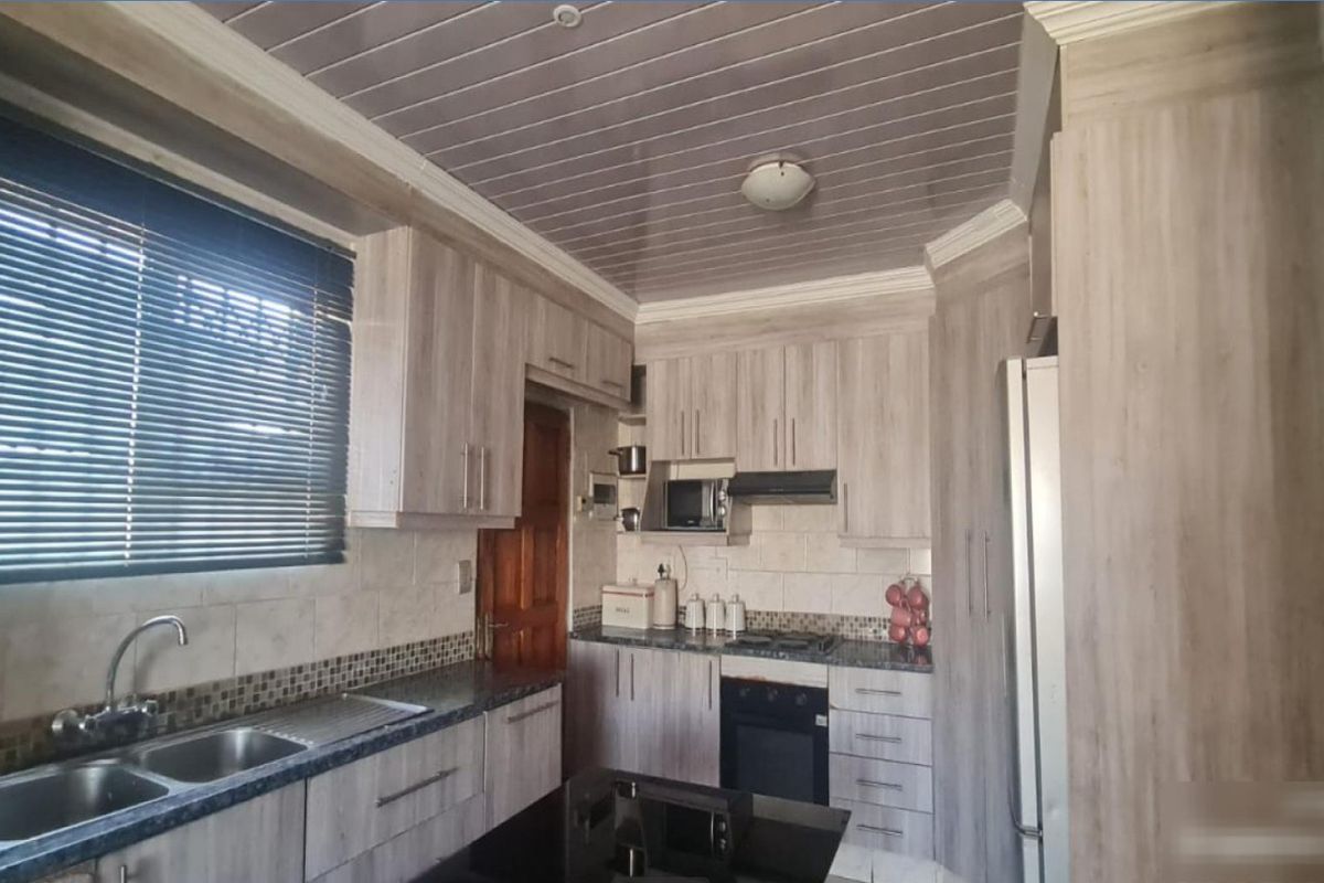 A functional kitchen featuring wood-look cabinetry, laminate countertops, a double basin sink, and integrated appliances including an oven, hob, and extractor fan.
