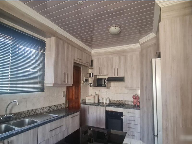 A functional kitchen featuring wood-look cabinetry, laminate countertops, a double basin sink, and integrated appliances including an oven, hob, and extractor fan.