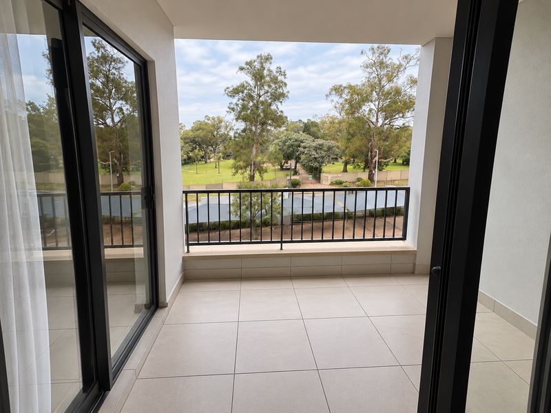 A clean, modern balcony featuring tiled flooring and a metal balustrade, offering an open view of the surrounding landscape.