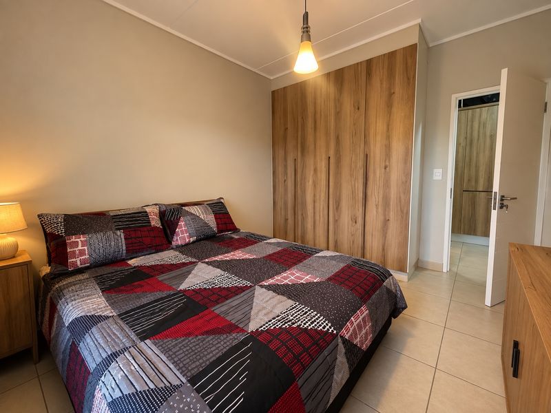 A well-maintained bedroom featuring neutral walls, tiled flooring, and floor-to-ceiling built-in wooden cupboards, with an adjacent view into a matching hallway.