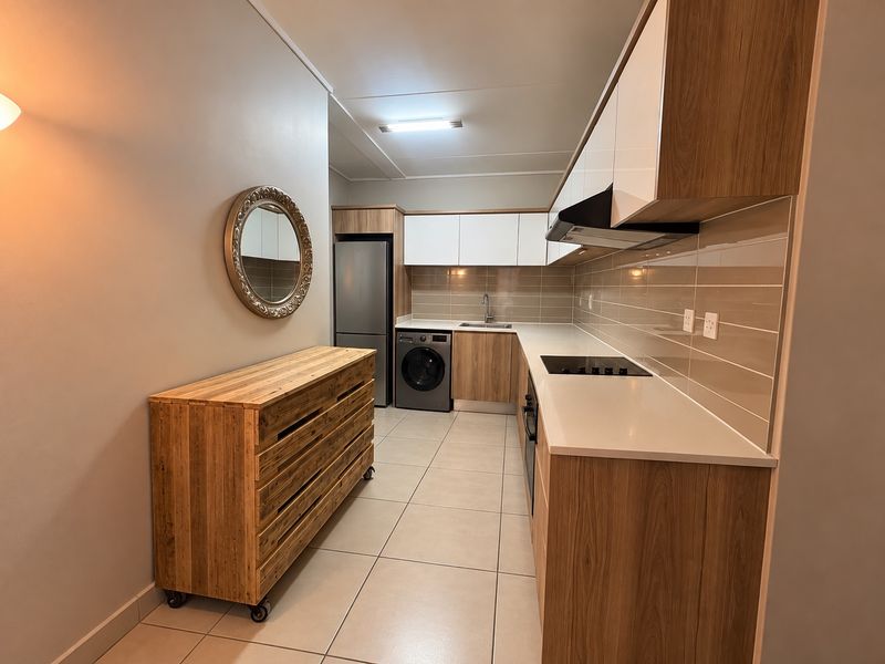 Modern galley-style kitchen featuring wood-grain cabinetry, stone countertops, integrated appliances, and neutral tiled flooring.