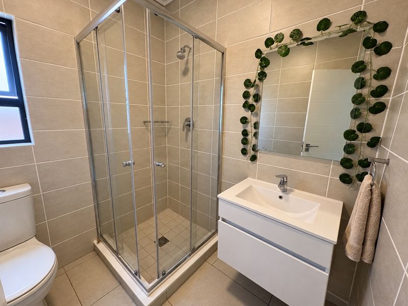 A modern bathroom featuring a glass shower enclosure, wall-mounted vanity with basin, and neutral floor-to-ceiling wall tiles.