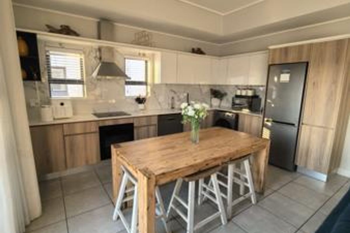 Modern kitchen featuring wood-finish cabinetry, marble-look backsplash, integrated appliances, and tiled flooring, offering a clean and functional culinary space.