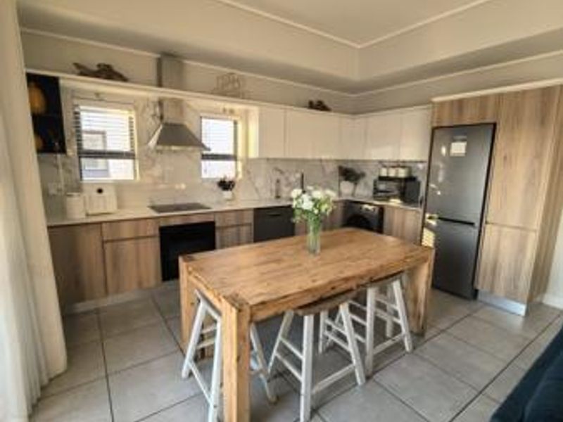 Modern kitchen featuring wood-finish cabinetry, marble-look backsplash, integrated appliances, and tiled flooring, offering a clean and functional culinary space.