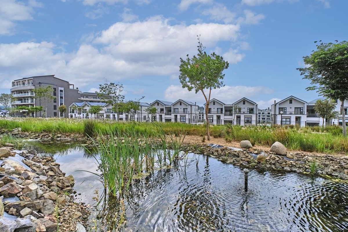 A scenic view of a residential apartment complex featuring a landscaped pond and water feature in the foreground.