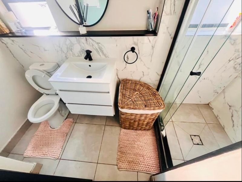 Modern bathroom featuring a vanity cabinet, toilet, and glass-enclosed shower with marble-look wall tiling and contemporary black fixtures.
