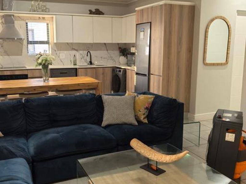 Modern open-plan living area featuring a contemporary kitchen with two-tone cabinetry, marble-look backsplash, and integrated appliances, seamlessly flowing into the lounge space.