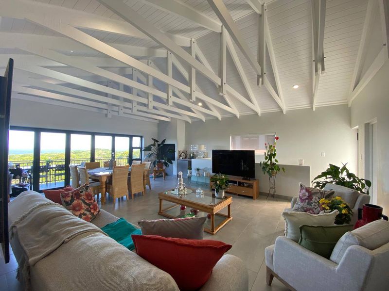 Spacious open-plan living and dining area featuring a striking vaulted ceiling with exposed white timber trusses, tiled floors, and large sliding doors to the balcony.