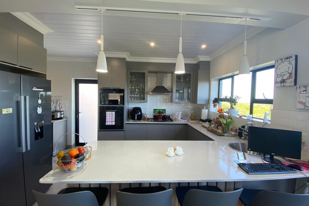Modern kitchen featuring a large quartz island, sleek grey cabinetry, built-in appliances, subway tile backsplash, and stylish pendant lighting.