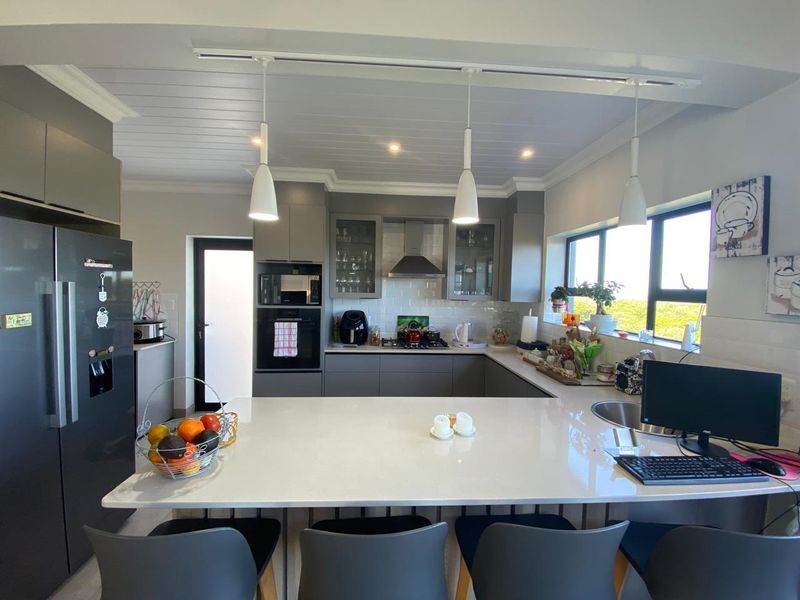 Modern kitchen featuring a large quartz island, sleek grey cabinetry, built-in appliances, subway tile backsplash, and stylish pendant lighting.