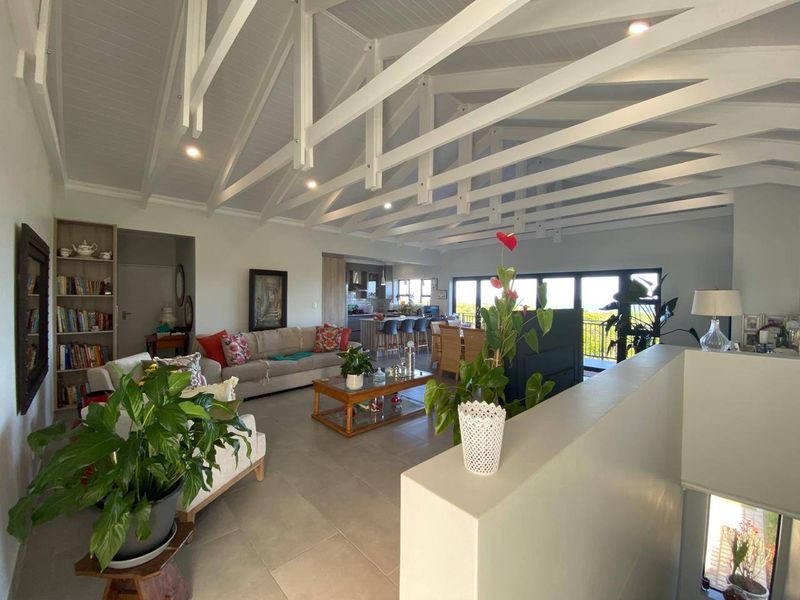 Spacious open-plan living area featuring a high vaulted ceiling with exposed white trusses, tiled floors, and large bi-fold doors leading to an outdoor space.