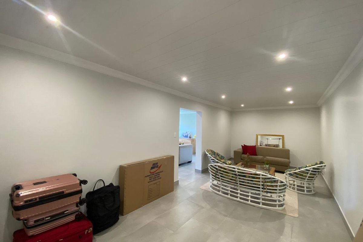 A spacious living room featuring modern tiled flooring, a clean tongue and groove ceiling, and recessed downlighting, offering a bright and neutral living space.