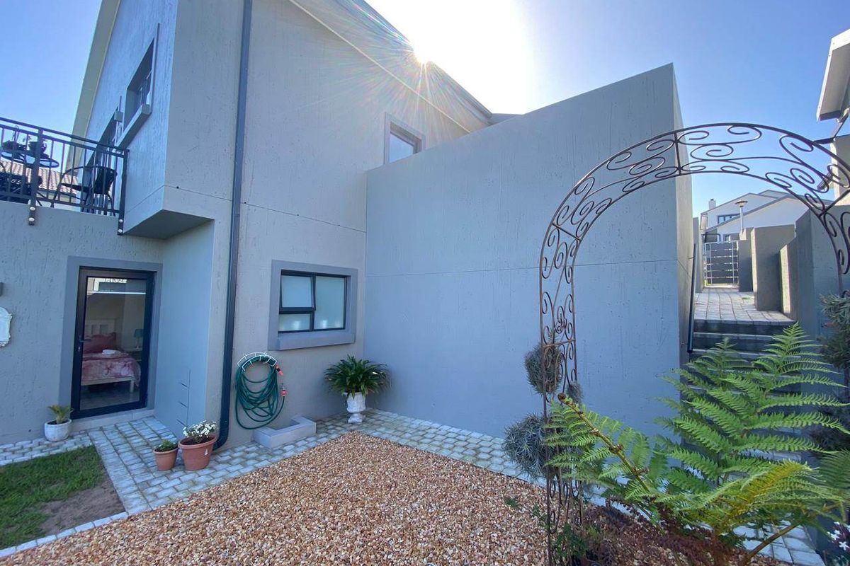 A well-maintained rear exterior view featuring a textured facade, gravel garden area, paved pathways, and an external staircase leading to an upper balcony.