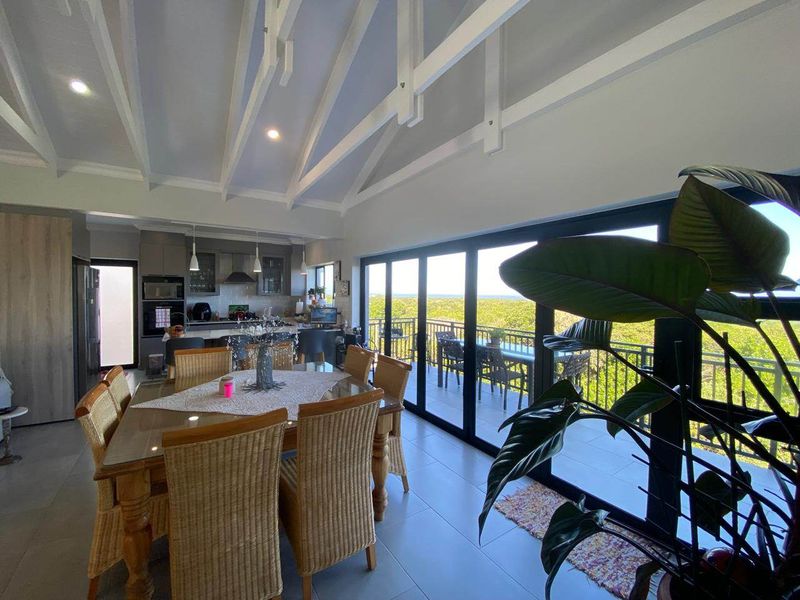 Spacious open-plan living and dining area featuring a vaulted ceiling with exposed rafters, modern kitchen, and large sliding doors opening to a scenic balcony.