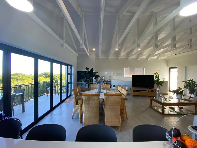 Spacious open-plan living and dining area featuring high vaulted ceilings with exposed beams, tiled floors, and large sliding doors opening onto a balcony.