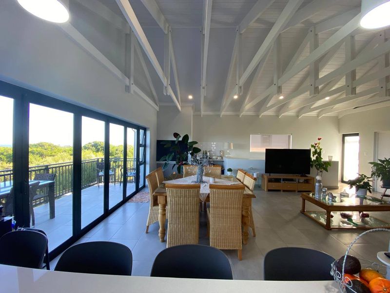 Spacious open-plan living and dining area featuring high vaulted ceilings with exposed rafters, large sliding doors to the balcony, and modern tiled flooring.