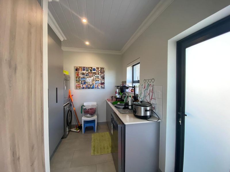 A functional laundry room featuring modern grey cabinetry, stone countertops, a sink, and direct access to the exterior via a frosted glass door.