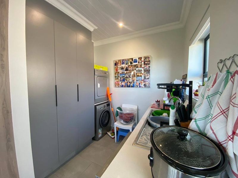 A functional laundry room featuring modern grey built-in cabinetry, a stainless steel sink, and tiled flooring with a clean, well-maintained finish.