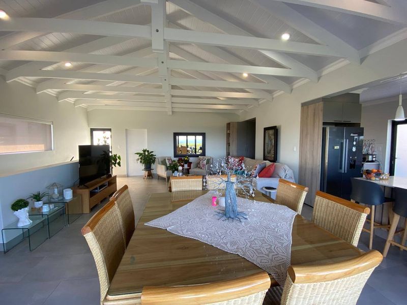 Spacious open-plan living and dining area featuring high vaulted ceilings with exposed beams, tiled floors, and a modern integrated kitchen.