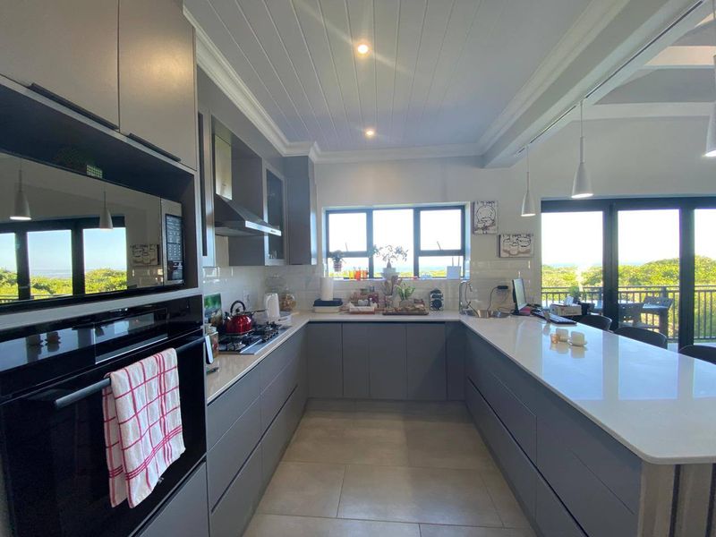 Modern kitchen featuring sleek grey cabinetry, quartz countertops, high-end built-in appliances, and a bright, open layout with views of the surrounding greenery.