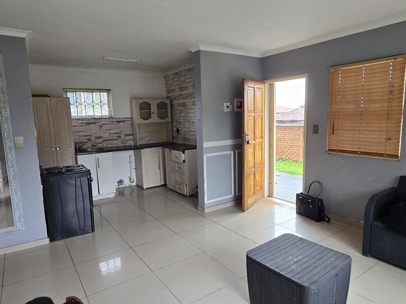 Open-plan living area featuring tiled floors, built-in kitchen cabinetry, and direct access to the exterior through a wooden door.