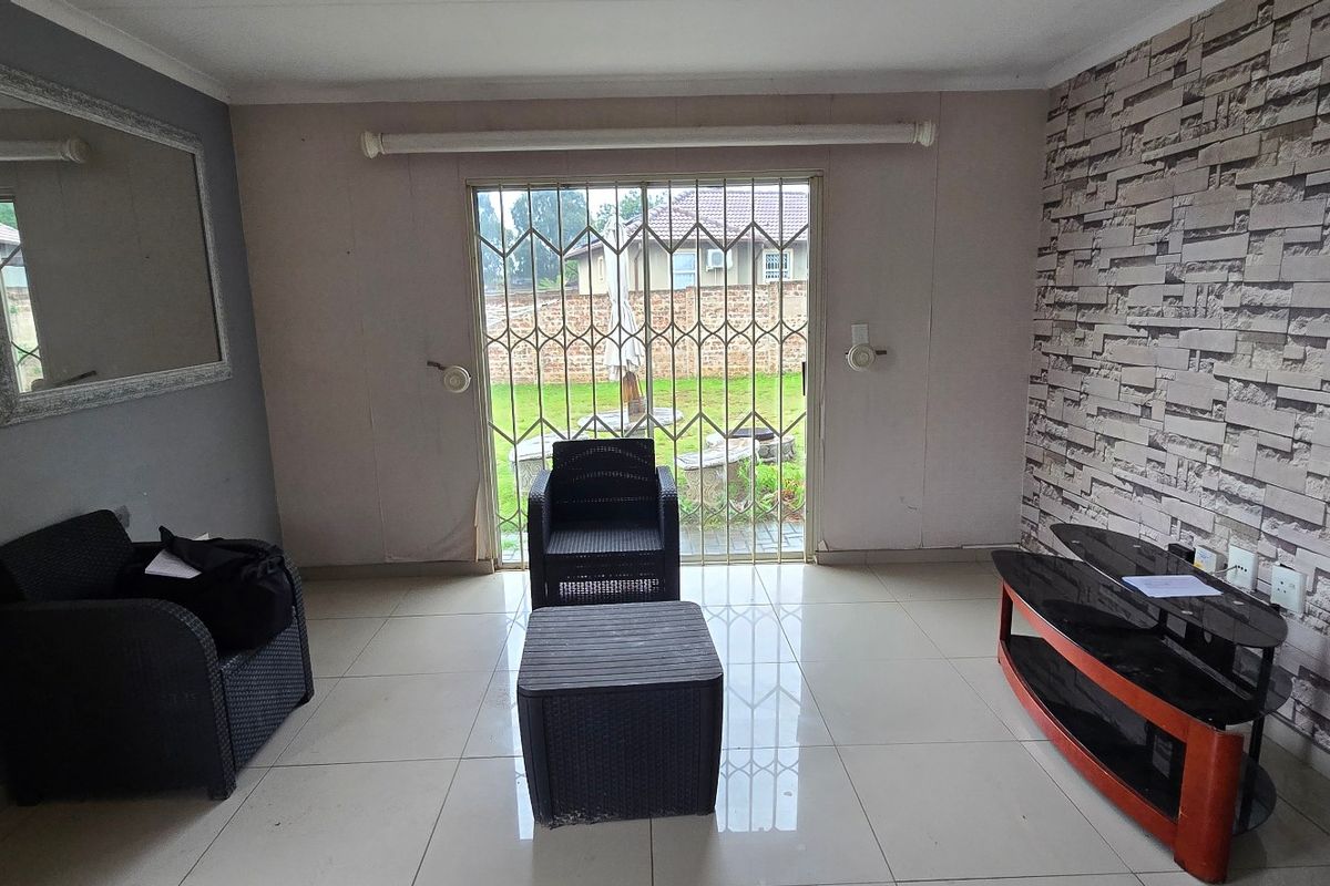 Living room featuring tiled flooring, a textured feature wall, and a sliding glass door with a security gate leading to the garden.