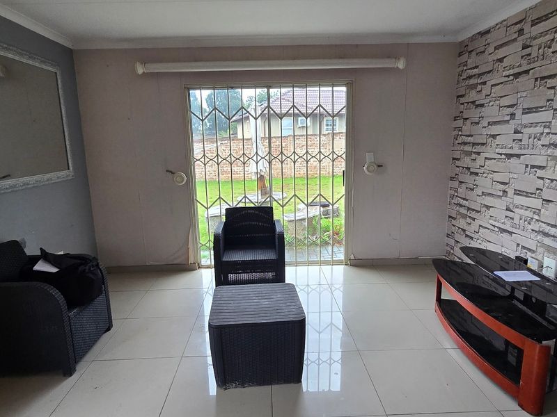 Living room featuring tiled flooring, a textured feature wall, and a sliding glass door with a security gate leading to the garden.
